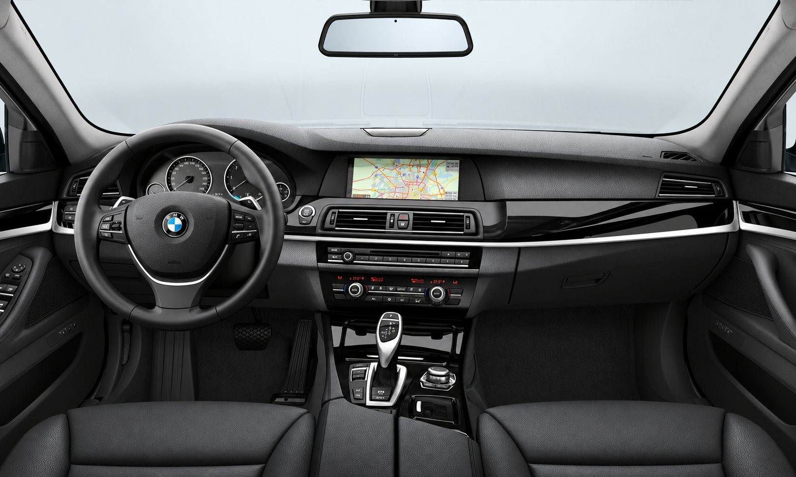 Vue intérieure du tableau de bord d'une BMW avec volant à logo BMW, écran de navigation central, console et sièges en cuir noir.